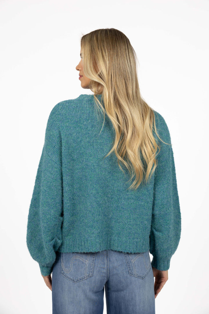 Person wearing a teal sweater and blue jeans on a white background