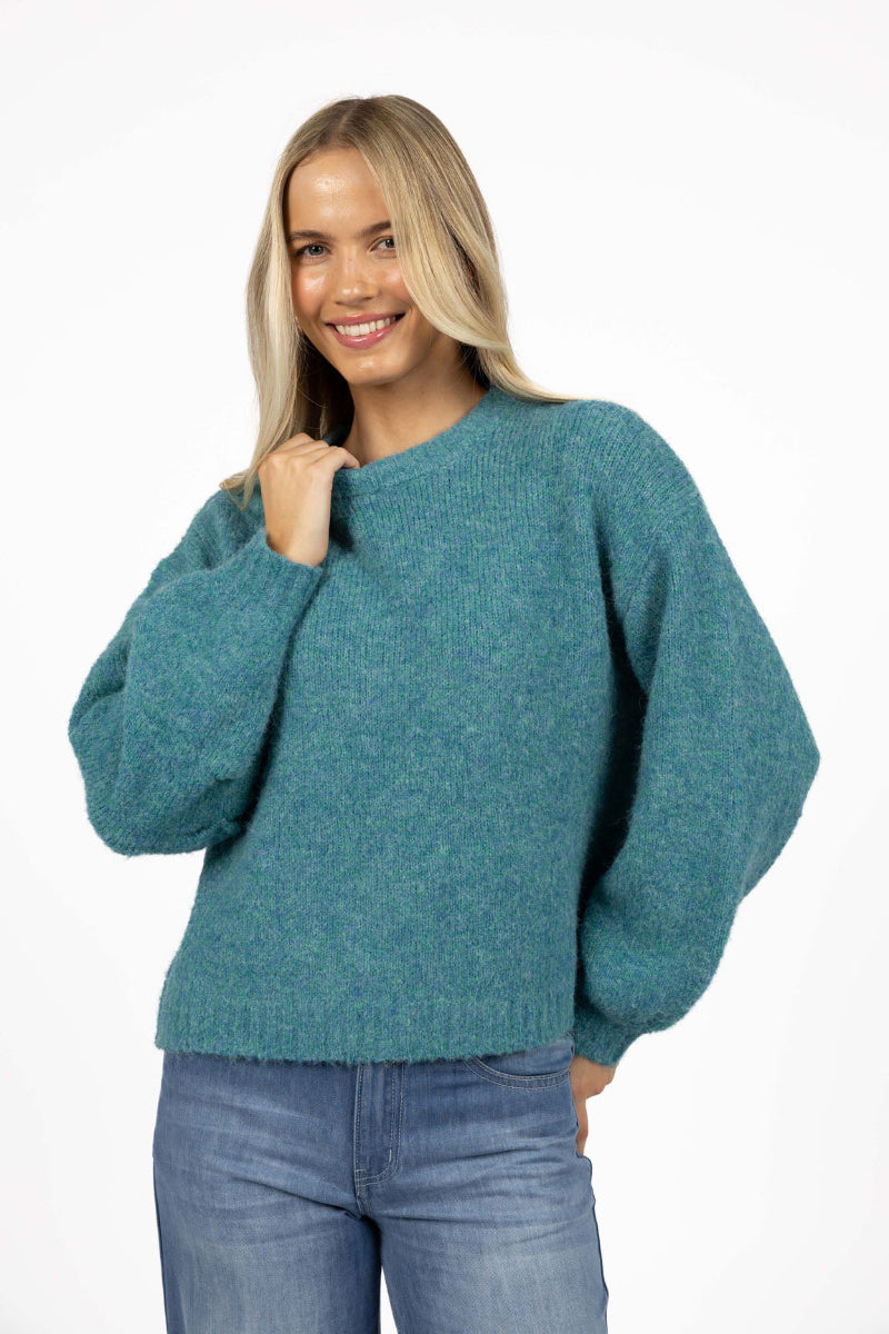 Woman wearing a teal sweater and blue jeans on a white background