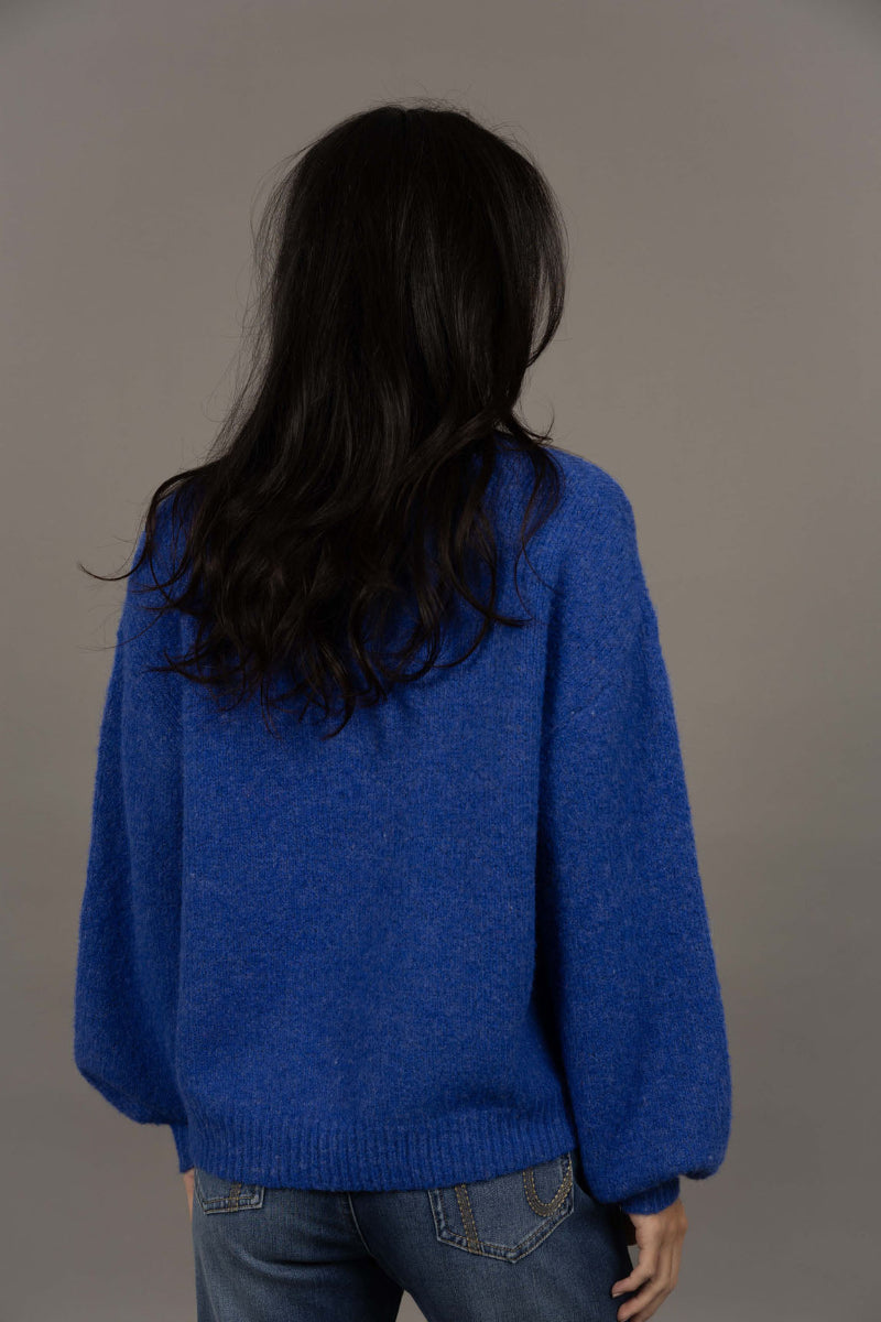 Person wearing a blue sweater and jeans against a gray background