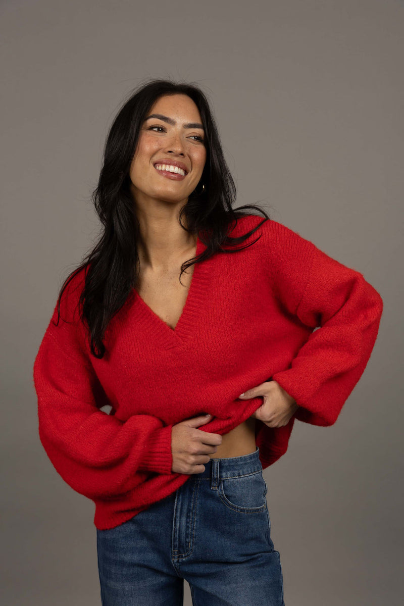 Woman wearing a red sweater and blue jeans against a gray background