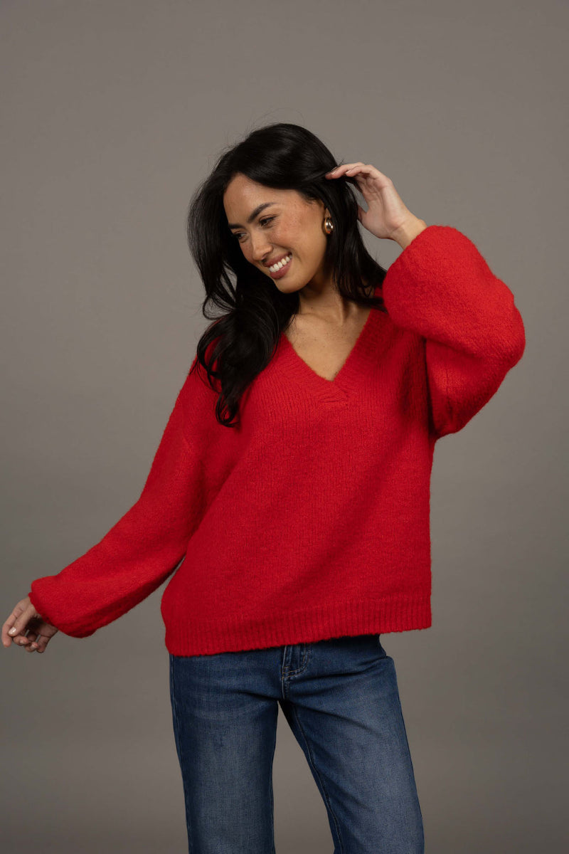 Woman wearing a red sweater and blue jeans against a gray background