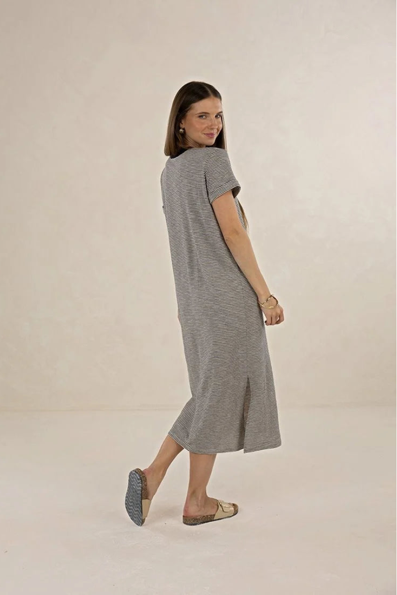 A woman modeling a short-sleeve, knee-length gray knit dress, photographed in a studio setting against a warm off-white background.