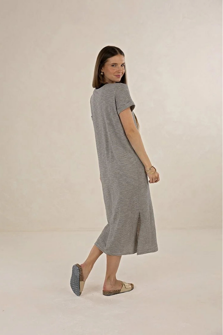 A woman modeling a short-sleeve, knee-length gray knit dress, photographed in a studio setting against a warm off-white background.