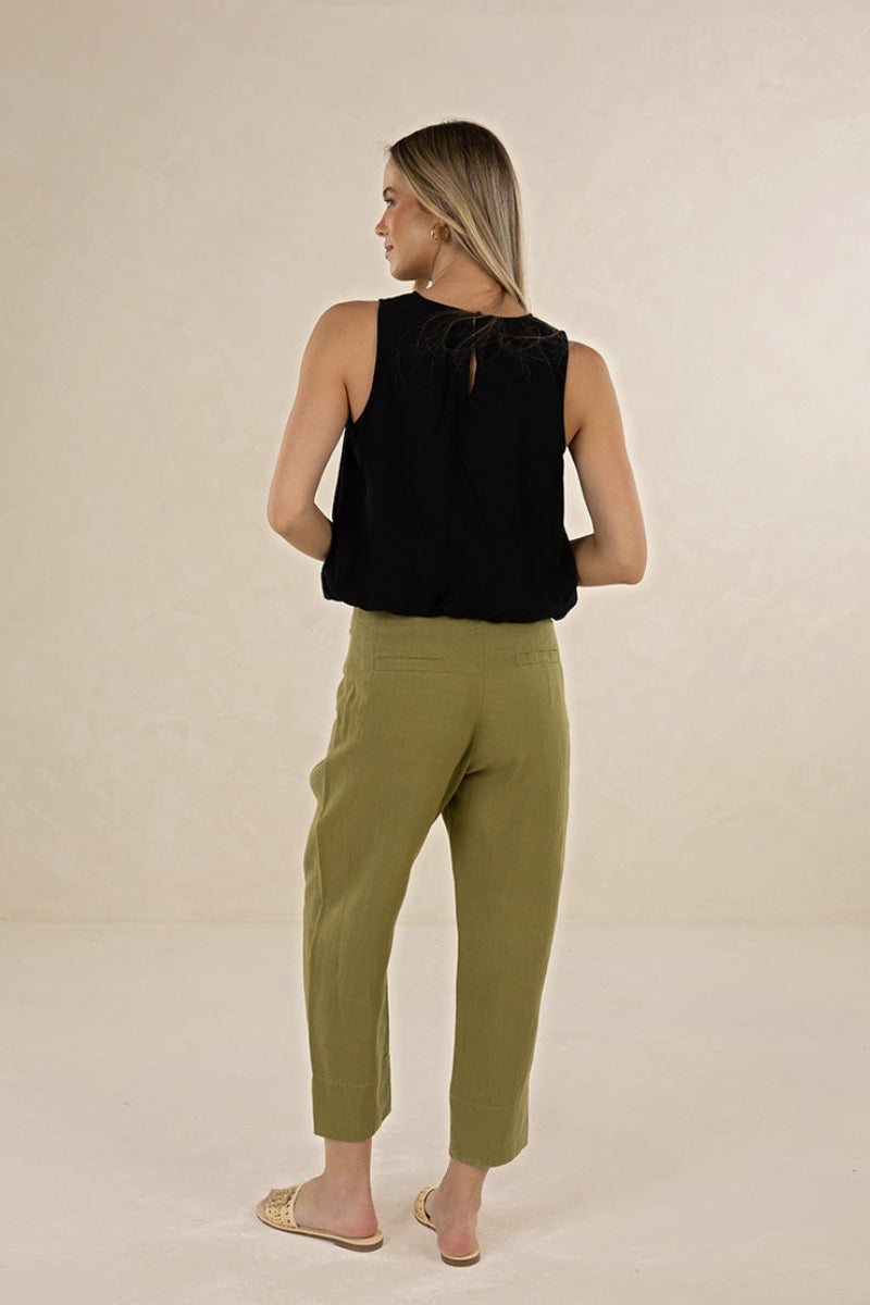Woman wearing a black sleeveless top and green pants on a beige background
