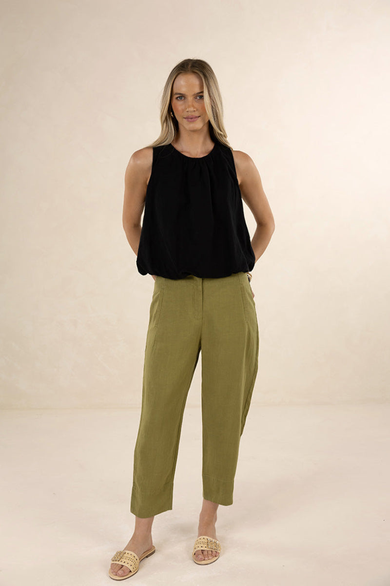 Woman wearing a black sleeveless top and green pants on a beige background