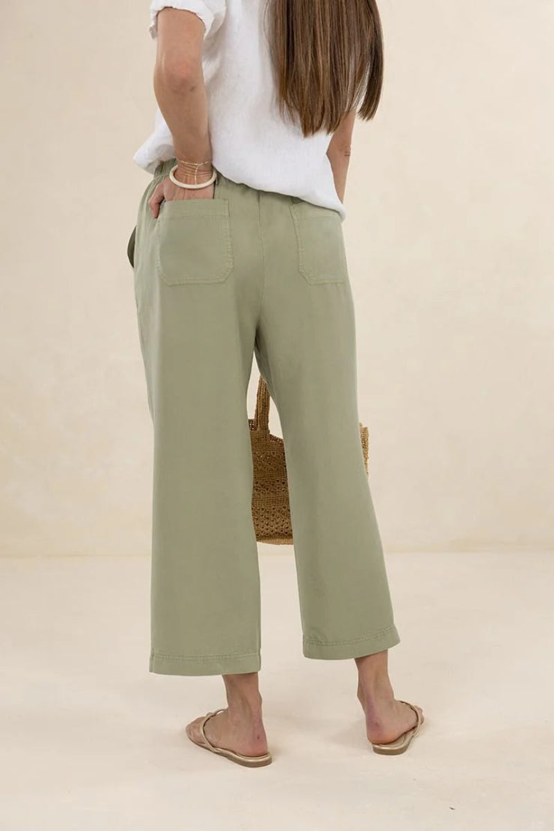 Person wearing light green pants and a white top on a beige background