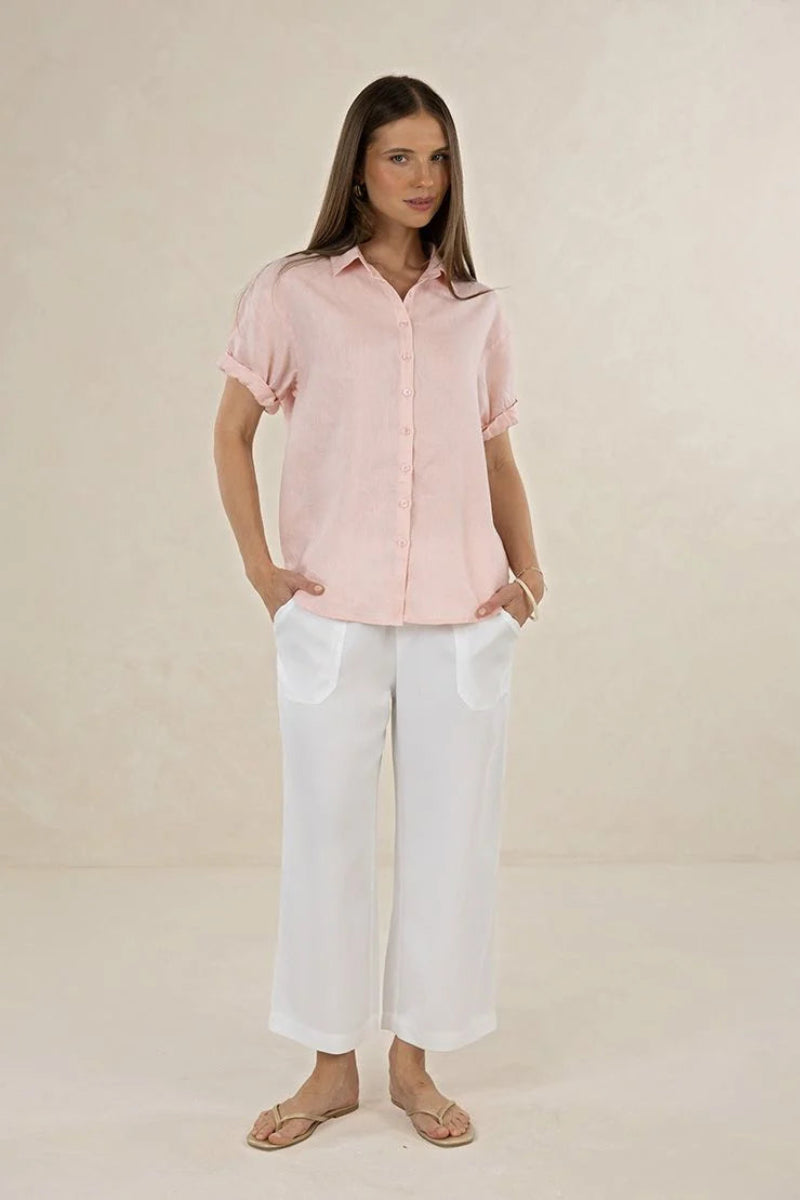 Woman wearing a light pink button-up shirt and white pants on a beige background