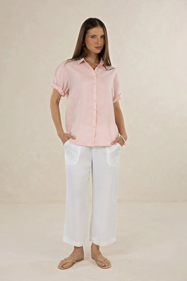 Woman wearing a light pink button-up shirt and white pants on a beige background
