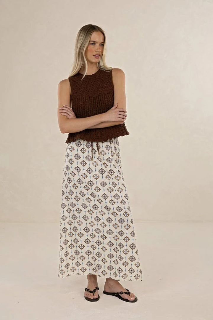 Woman wearing a brown sleeveless top and patterned skirt on a beige background