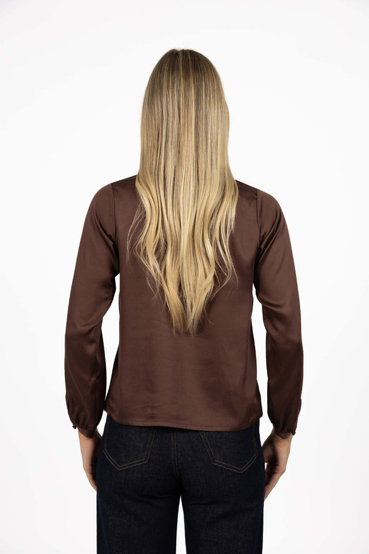Person wearing a brown long-sleeve top and dark jeans on a white background