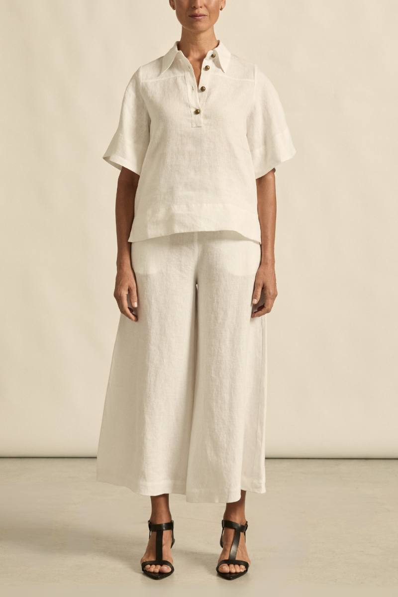 This front view of the Insinuate Top in Porcelain showcases its sharp tailored fit, flutter sleeves, crisp collar, and elegant brass domed buttons.
