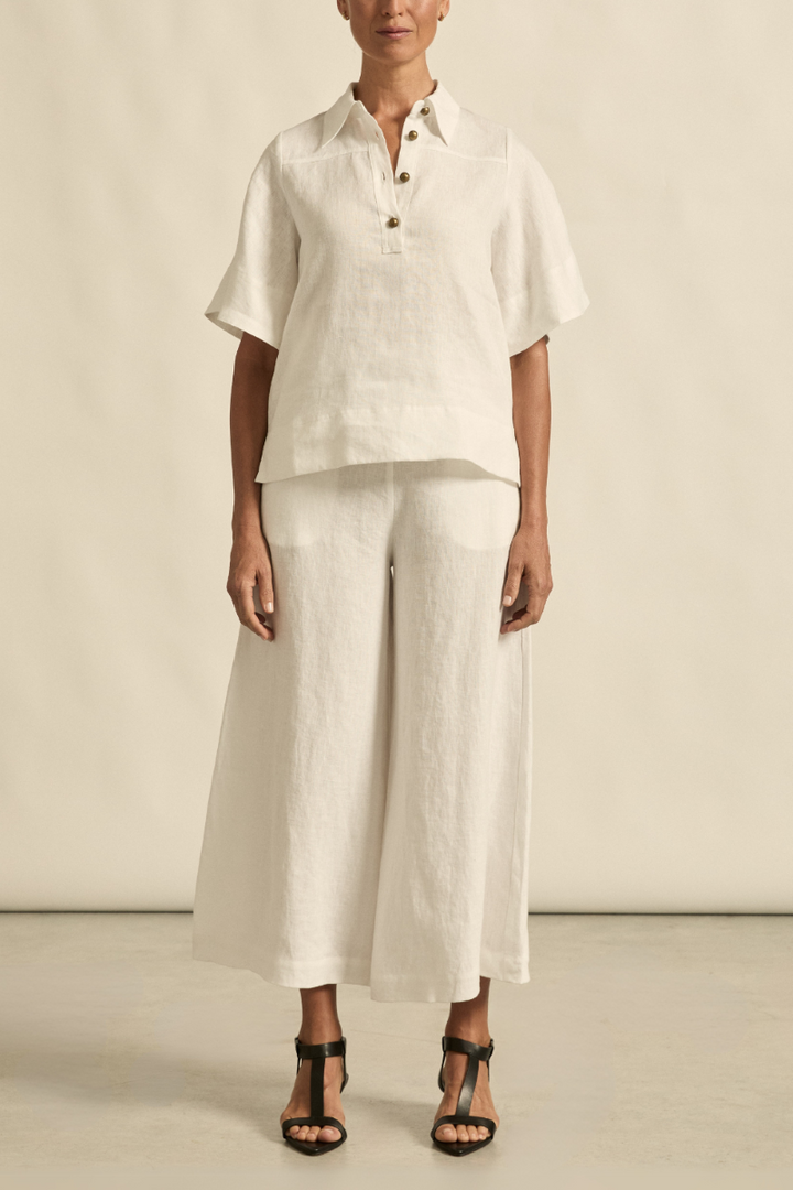 This front view of the Insinuate Top in Porcelain showcases its sharp tailored fit, flutter sleeves, crisp collar, and elegant brass domed buttons.
