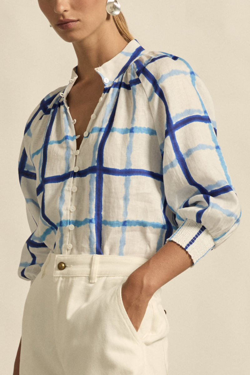 This side close-up image of the Inspire Top in Azure Check highlights the soft drape of the linen fabric, elasticated rouleau loops, and the gentle curve of the high stand collar.

