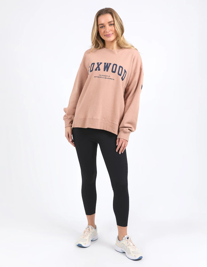 Women wearing a relaxed fir tan Foxwood interval crew sweatshirt with black leggings in a neutral background.