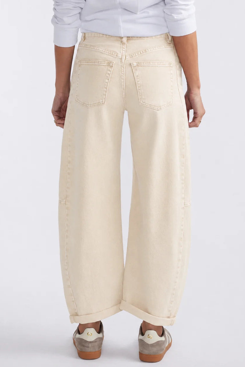 Back view of a person wearing off-white wide-leg cropped jeans with a white shirt and brown sneakers, shown against a light gray studio background.