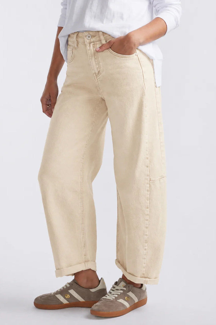 A person wearing loose, wide-leg beige denim jeans with a white top and brown sneakers, shown from the waist down against a light gray studio background.