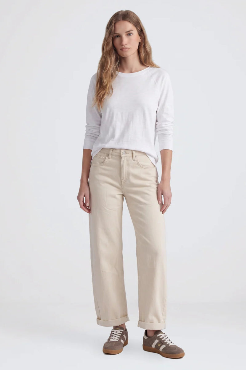 A woman modeling a white long-sleeve crewneck shirt, beige wide-leg cropped pants, and brown sneakers against a plain white studio background.