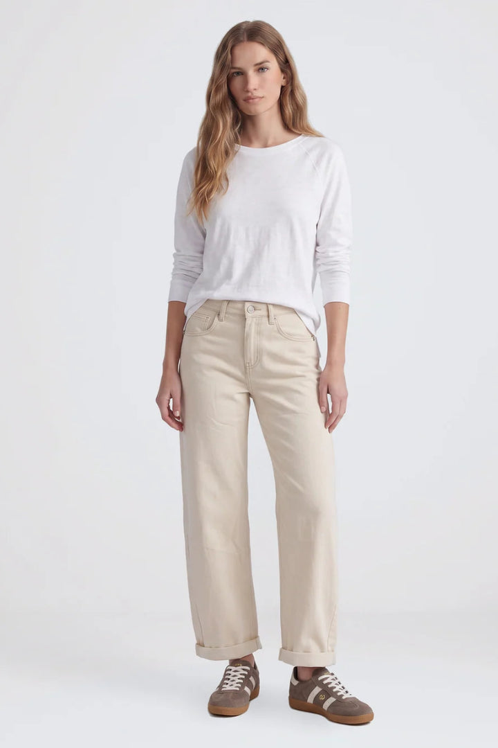 A woman modeling a white long-sleeve crewneck shirt, beige wide-leg cropped pants, and brown sneakers against a plain white studio background.