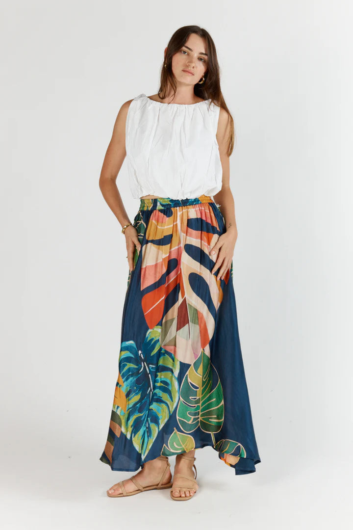 Woman wearing a white top and colorful tropical print skirt on a white background