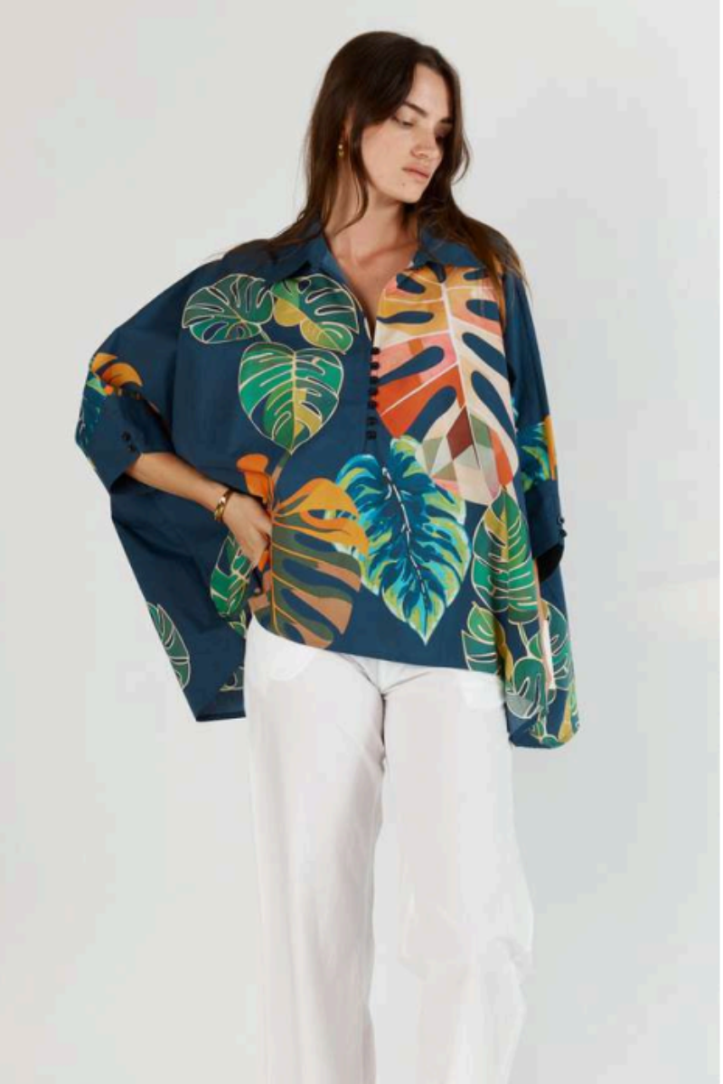 Woman wearing a colorful tropical leaf patterned shirt against a white background