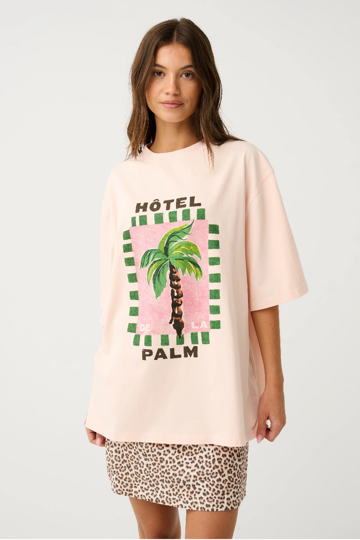 Woman wearing a light pink oversized t-shirt with a palm tree design and leopard print shorts on a white background