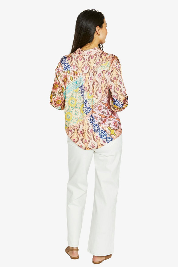 Woman wearing a colorful patterned blouse and white pants on a white background