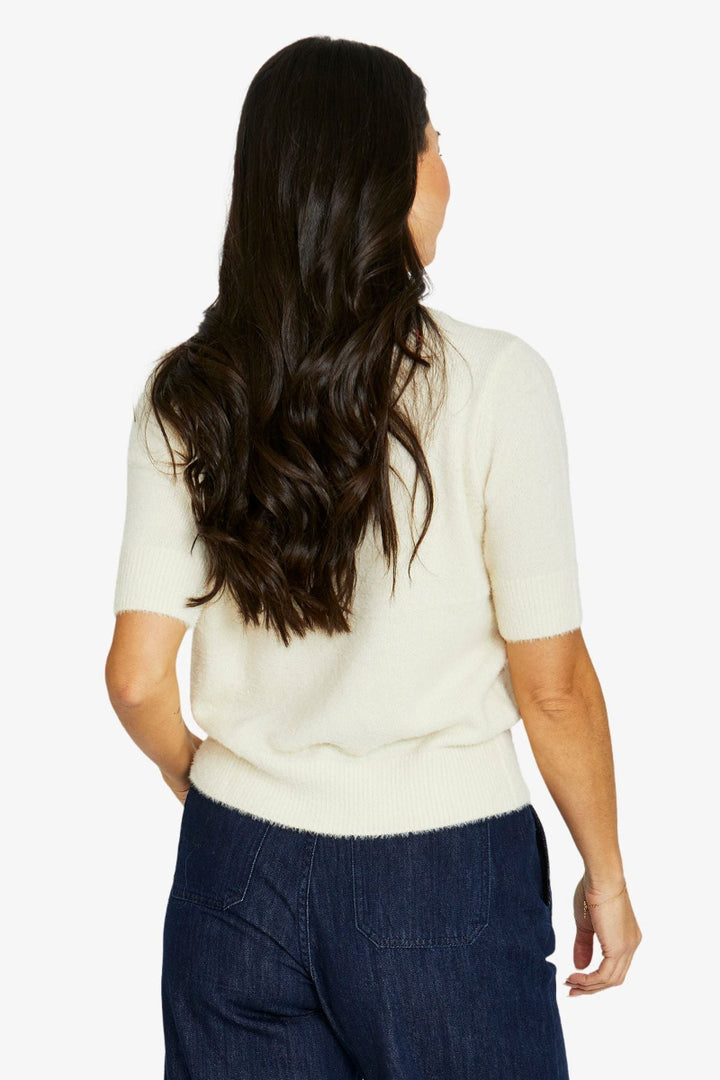 Woman wearing a cream sweater and dark blue pants on a white background