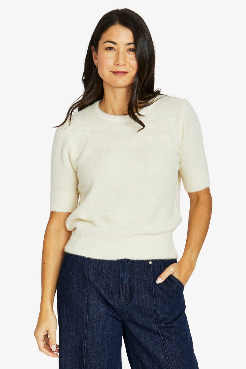 Woman wearing a white sweater and dark blue pants on a white background