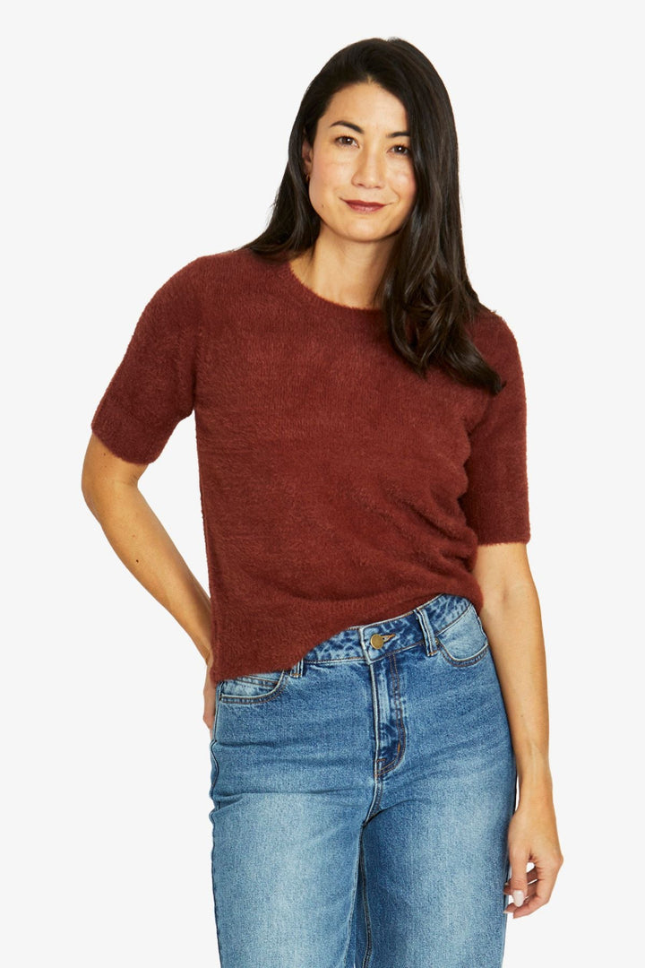 Woman wearing a maroon sweater and blue jeans on a white background