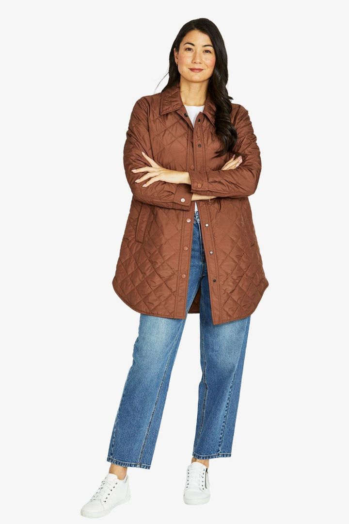 Woman wearing a brown quilted jacket and blue jeans on a white background
