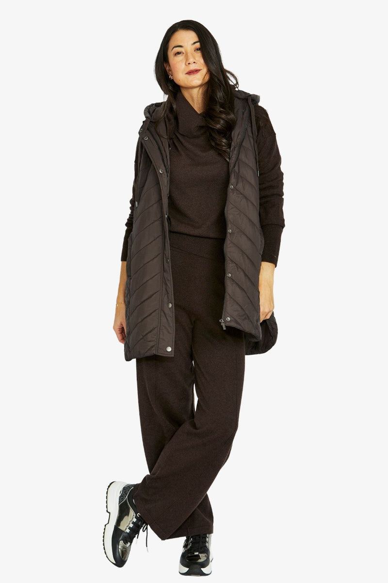 Woman wearing a dark brown outfit with a puffer vest on a white background