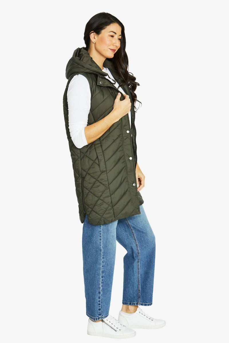 Woman wearing a green quilted vest over a white shirt with blue jeans on a white background