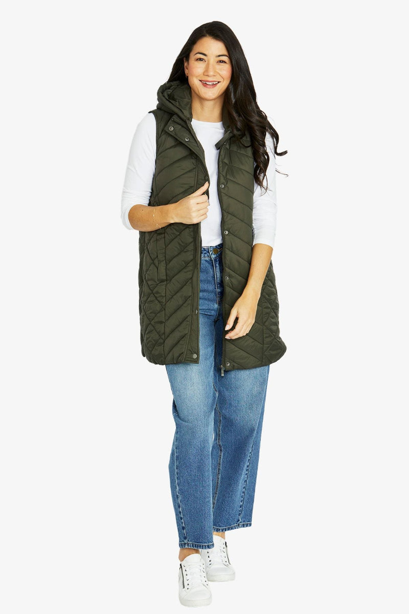 Woman wearing a green puffer vest over a white shirt with blue jeans on a white background