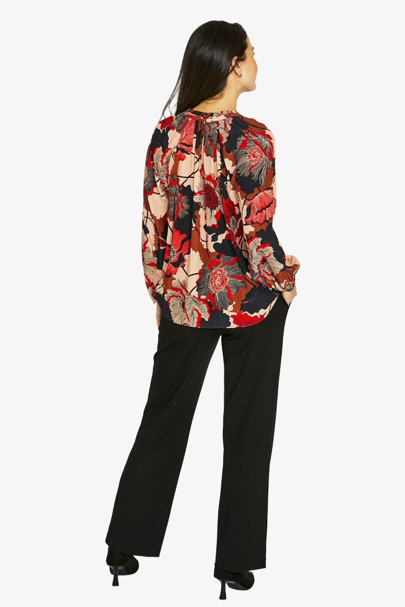 Woman wearing a colorful floral blouse and black pants on a white background