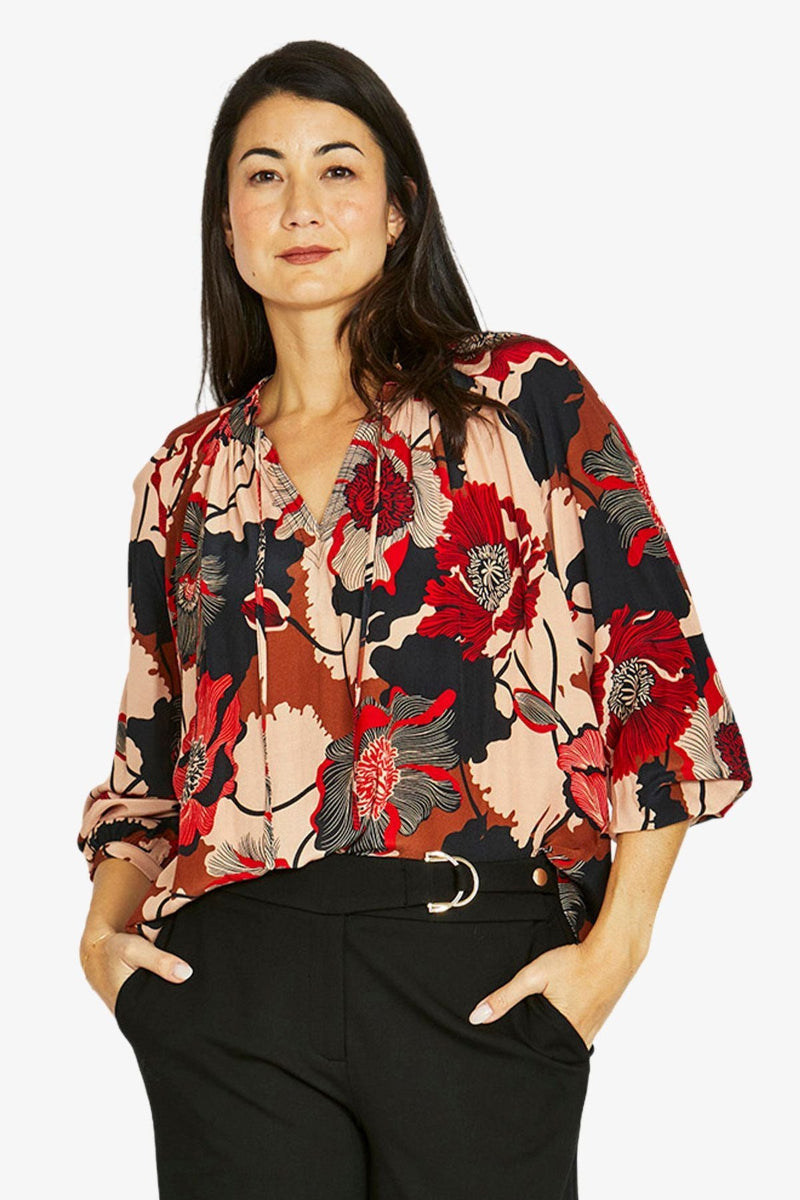 Woman wearing a colorful floral blouse with black pants on a white background
