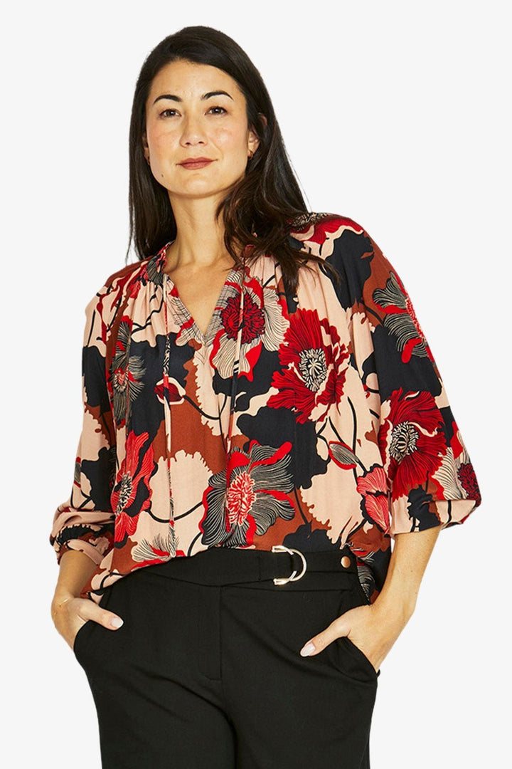 Woman wearing a colorful floral blouse with black pants on a white background