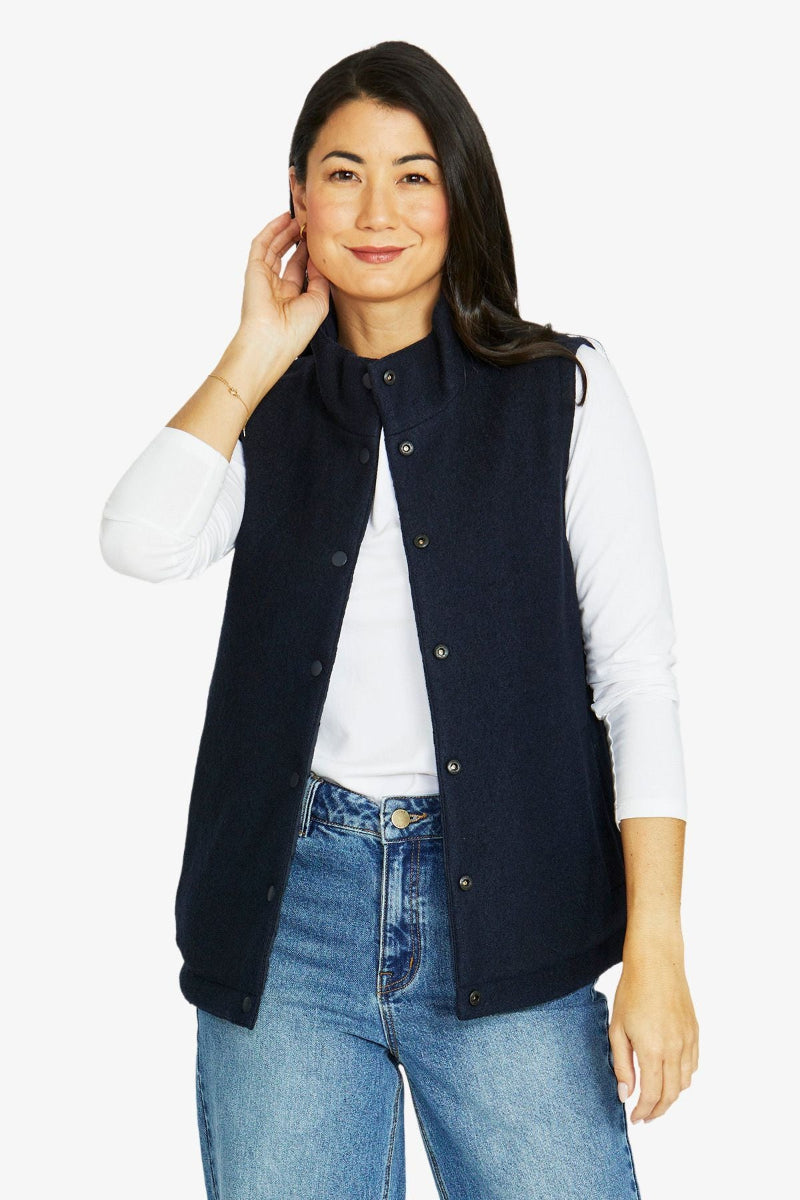 Woman wearing a navy vest over a white shirt and blue jeans on a white background
