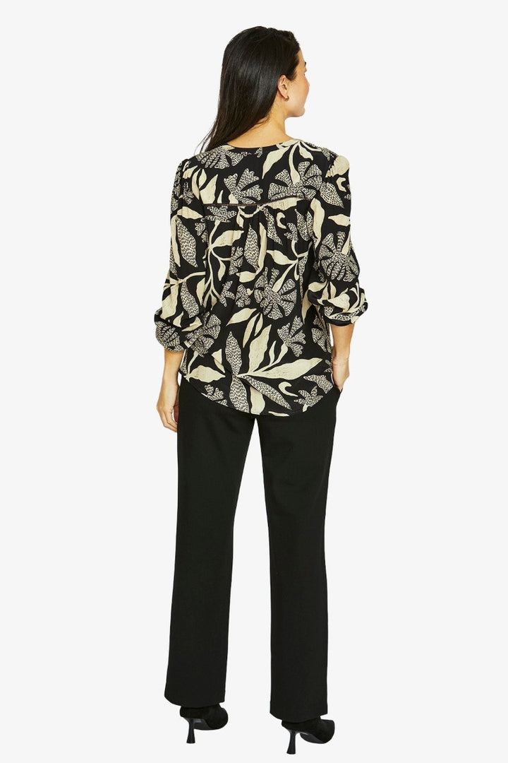 Woman wearing a black and beige patterned blouse with black pants on a white background