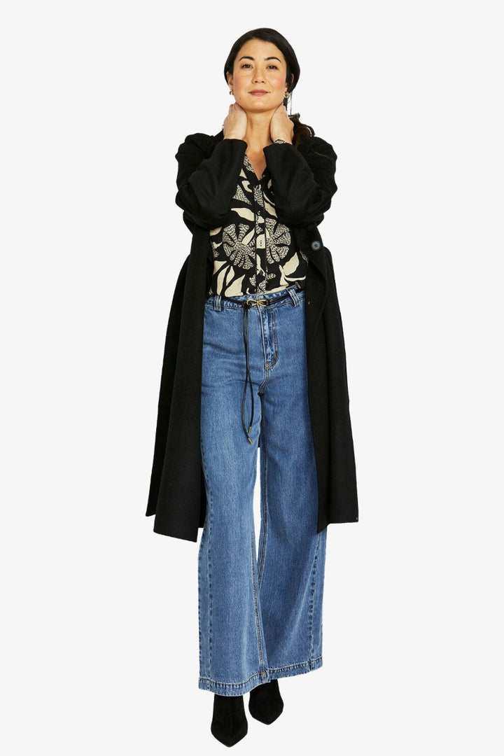 Person wearing a black coat, patterned top, and blue jeans on a white background