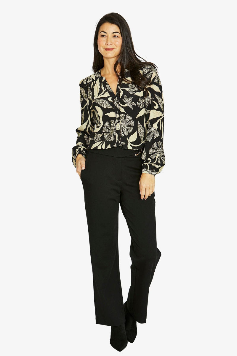 Woman wearing a patterned blouse and black pants on a white background