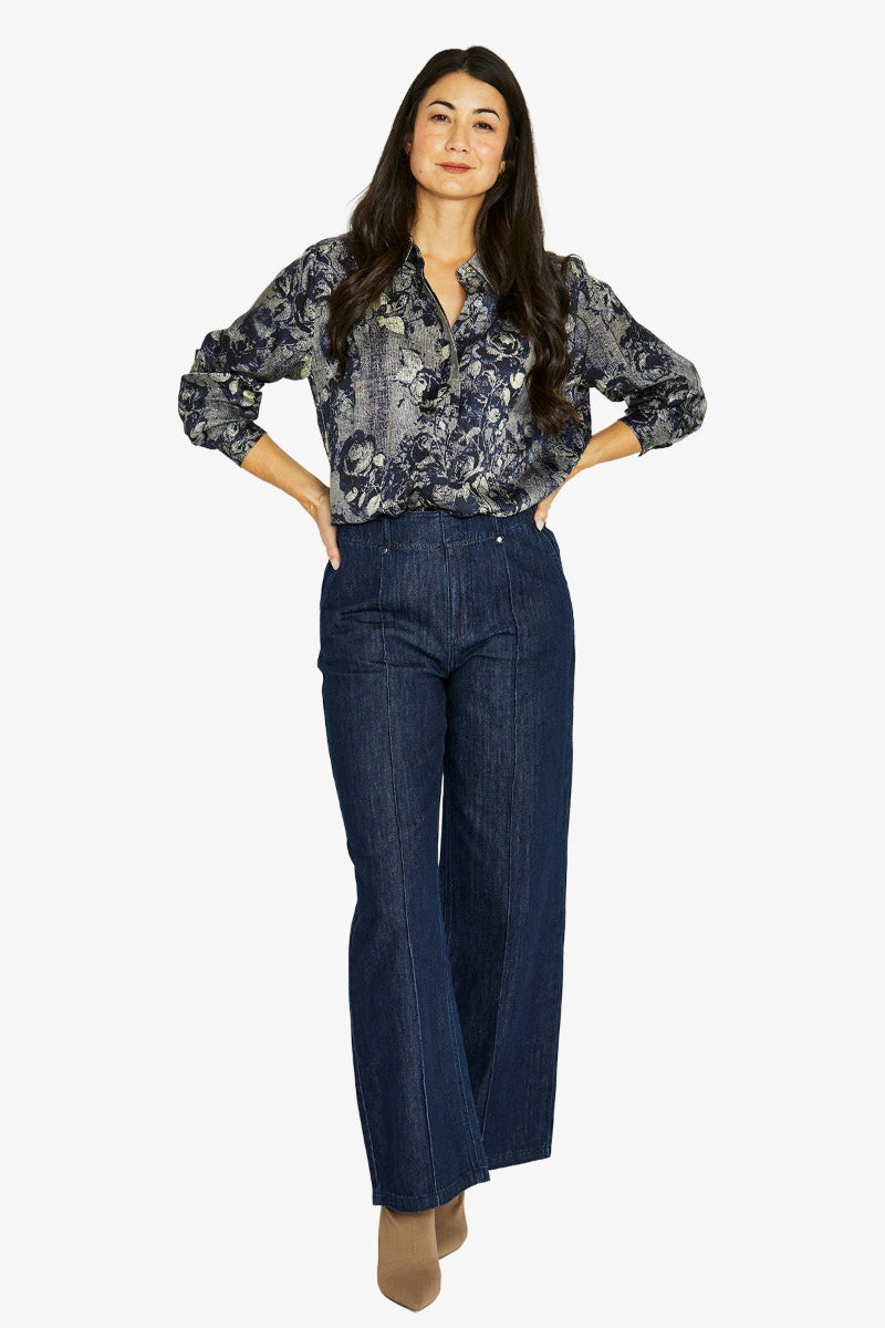 Woman wearing a floral blouse and dark jeans on a white background