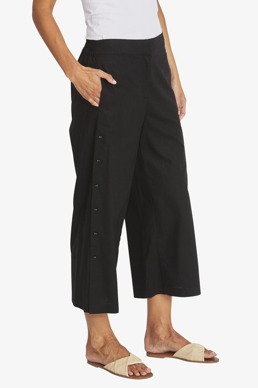 Person wearing black wide-leg pants with buttons on a white background