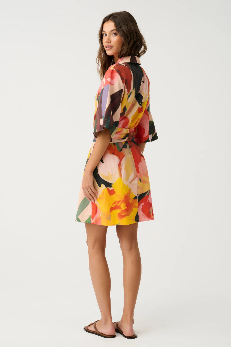 Woman wearing a colorful floral mini dress on a white background.Dress features a fabric waist tie, three-quarter sleeves and a v neckline.