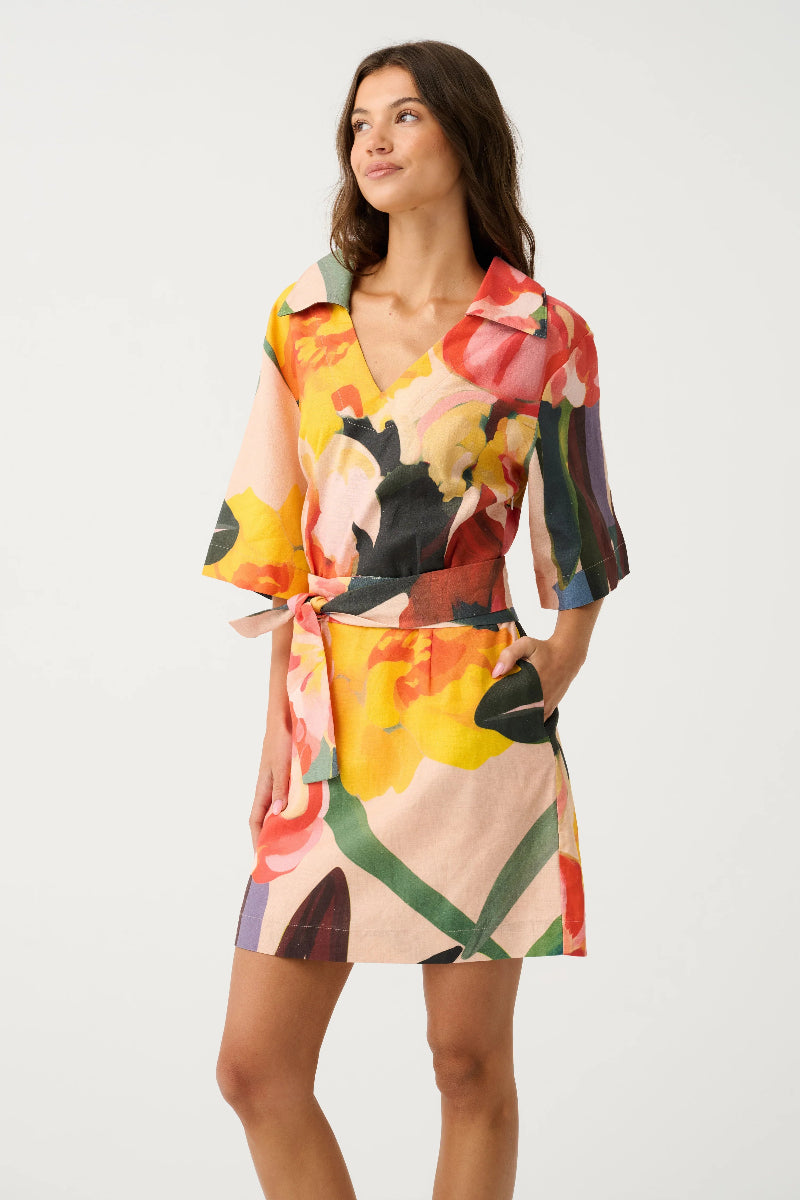 Woman wearing a colorful floral mini dress on a white background.Dress features a fabric waist tie, three-quarter sleeves and a v neckline.