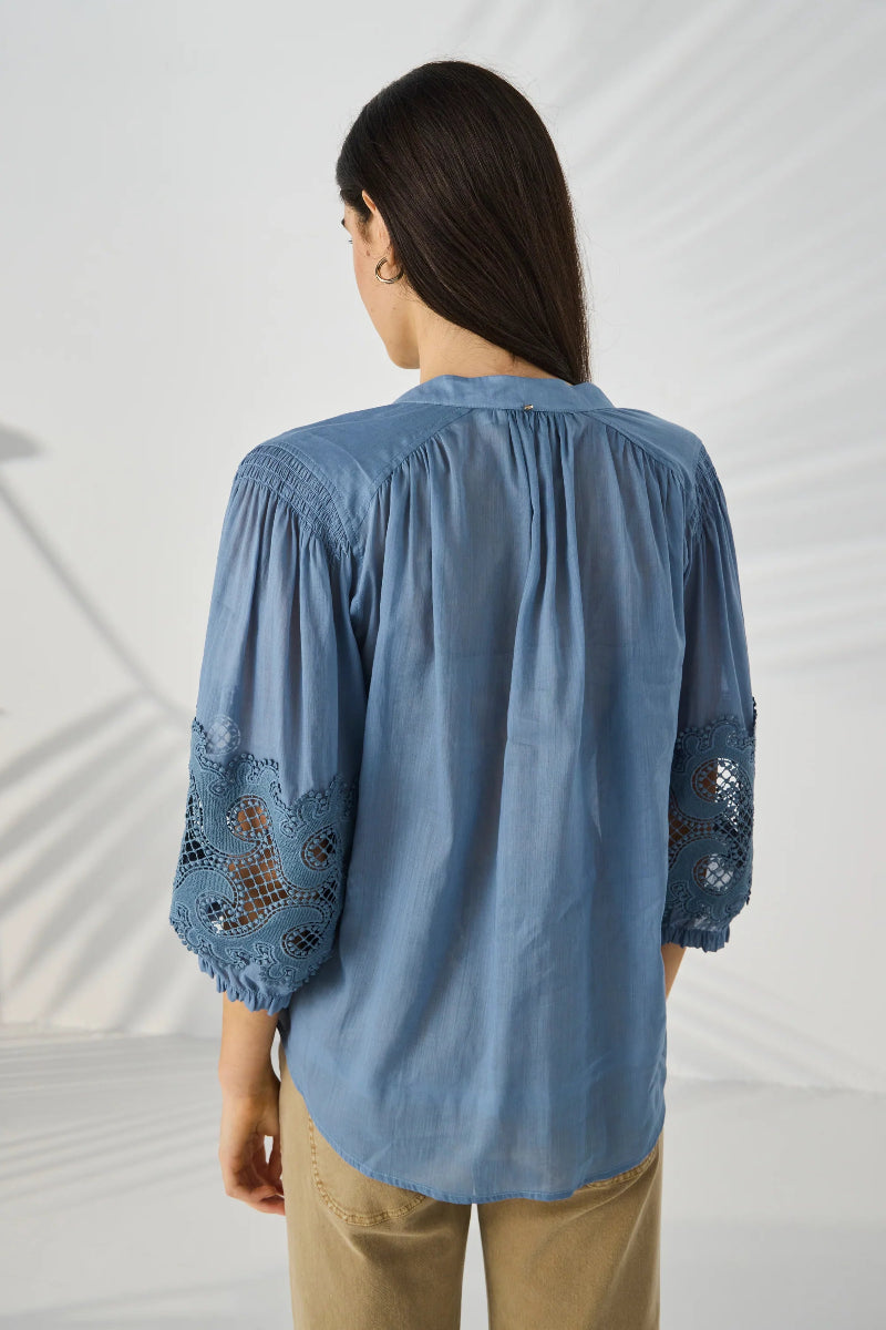 Woman wearing a blue blouse with lace details on a white background