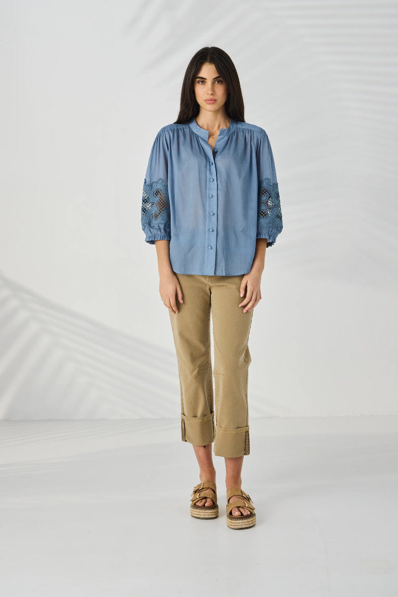 Woman wearing a blue shirt with lace details and beige pants on a white background