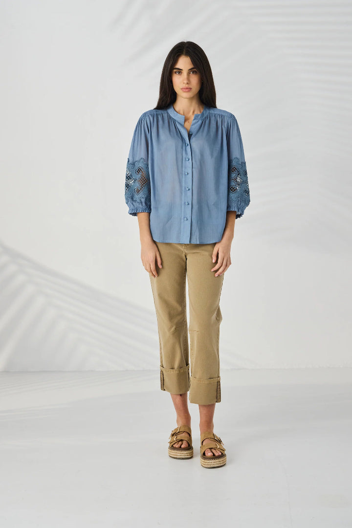 Woman wearing a blue shirt with lace details and beige pants on a white background