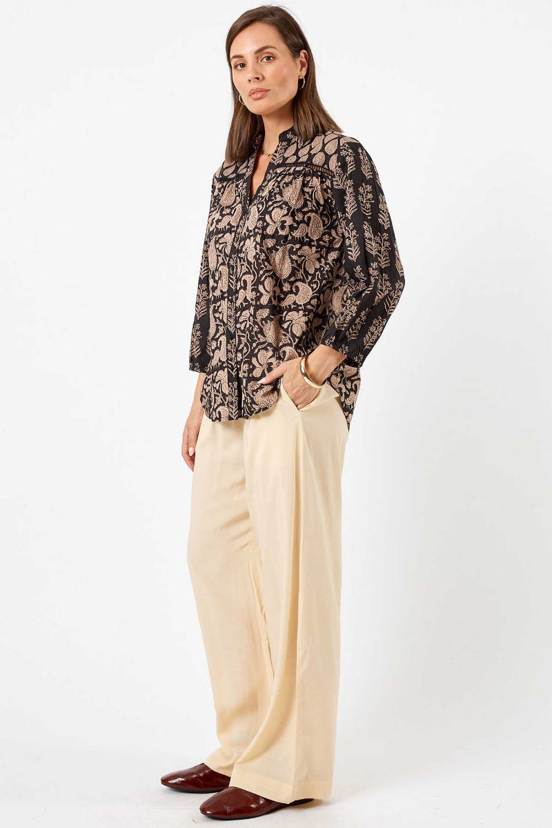 Woman wearing a patterned blouse and beige pants on a white background
