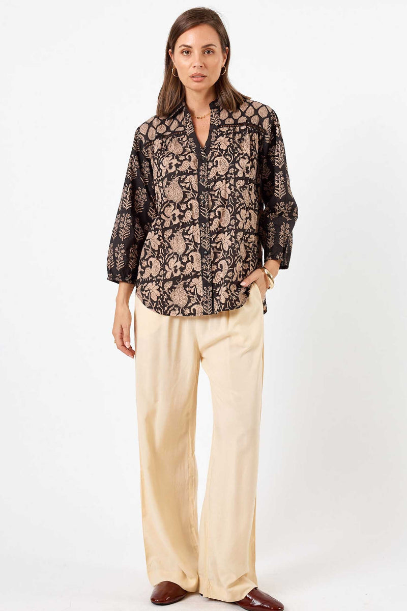 Woman wearing a patterned blouse and beige pants on a white background