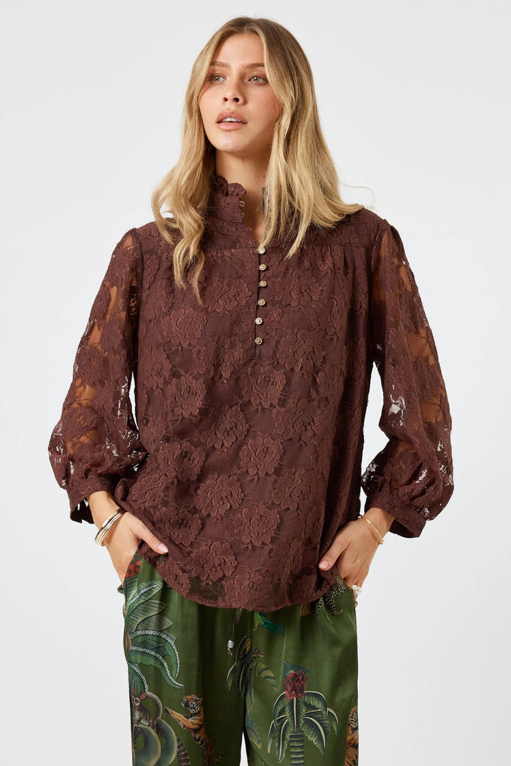 Woman wearing a brown lace blouse and green pants with floral patterns on a white background